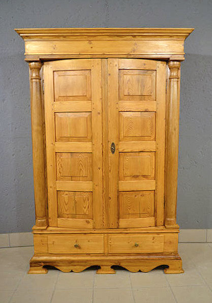 Antiker Roskildeschrank aus dem Biedermeier um 1840 aus massivem Kiefernholz mit bauchigen T&uuml;ren und Halbs&auml;ulen. Wir liefern zuverl&auml;ssig, kosteng&uuml;nstig und pers&ouml;nlich deutschlandweit bis in Ihr Zuhause. Nach Terminvereinbarung ist eine Besichtigung im M&ouml;bellager in Bargfeld-Stegen m&ouml;glich.