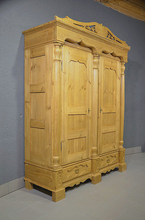 Linke Seitenansicht des antiken Gründerzeit Kleiderschranks aus massivem Kiefernholz mit Kassettenfüllung und profilierter Kranzleiste. Lieferung und Aufbau erfolgen persönlich und kostengünstig deutschlandweit.
