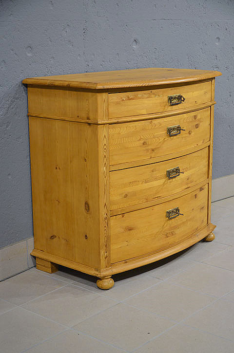 Linke Seitenansicht der antiken restaurierten Jugendstil Kommode aus massiver Kiefer mit harmonischer Linienfuehrung und warmer Honigfarbe. Wir liefern zuverl&auml;ssig, kosteng&uuml;nstig und pers&ouml;nlich &ndash; deutschlandweit bis in Ihr Zuhause. Nach Terminvereinbarung k&ouml;nnen Sie dieses M&ouml;belst&uuml;ck gerne in unserem M&ouml;bellager in Bargfeld-Stegen besichtigen.